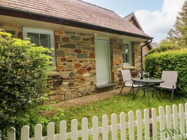 A stone cottage with two windows a door and outdoor table and chairs behind a white picket fence at Ty Rhydd in Newport Pembrokeshire
