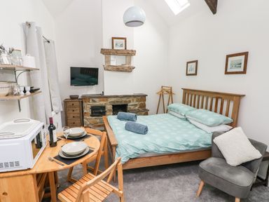 A bedroom with a wooden bed dining table with microwave and chairs a fireplace and a gray armchair at Ty Rhydd Newport Pembrokeshire