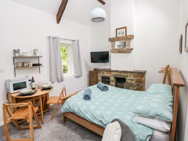 A bedroom with a bed towels a small dining table chairs a microwave and a fireplace at Ty Rhydd in Newport Pembrokeshire