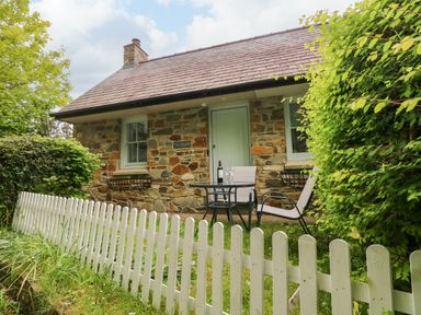 A stone cottage with a small garden table and chairs behind a white picket fence at Ty Rhydd in Newport Pembrokeshire