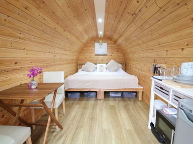 An arched wooden interior with a bed at the end a table with chairs on the left and a small kitchen area on the right at The Pod at Bank House Farm The Blythe near Hixon