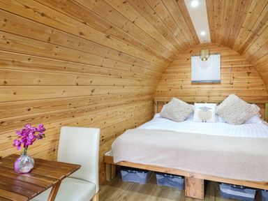 A bedroom with a wooden bed and a small table with a flower vase at The Pod at Bank House Farm The Blythe near Hixon