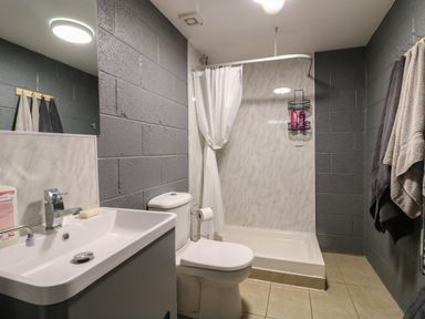A bathroom with a sink, toilet, shower area with curtain and towels hanging on wall at The Pod at Bank House Farm The Blythe near Hixon