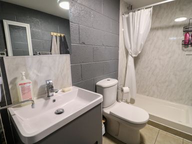 A bathroom with a sink, toilet, shower area with curtain, and towels on hooks at The Pod at Bank House Farm The Blythe near Hixon