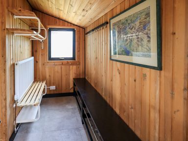 A wooden room with a window a radiator a shelf with hooks a long bench and framed artwork at Greengarth in Yanwath near Penrith