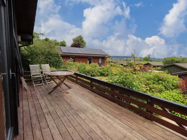 An outdoor wooden deck with two chairs and a table overlooking a garden and several houses with solar panels at Greengarth in Yanwath near Penrith