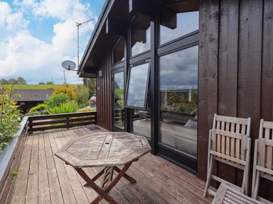 A wooden deck with a round wooden table and folded chairs outside a building with large glass windows at Greengarth in Yanwath near Penrith