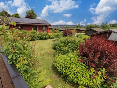 A garden with various bushes and plants in front of wooden houses with solar panels on the roof at Greengarth Yanwath near Penrith