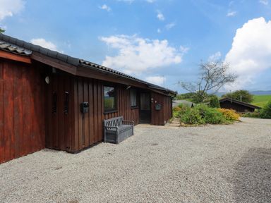 An exterior view of a wooden building with a bench on a gravel pathway and green shrubs and trees nearby at Greengarth in Yanwath near Penrith