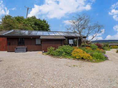 A brown wooden house with solar panels on the roof gravel driveway and various plants and shrubs in the garden at Greengarth in Yanwath near Penrith