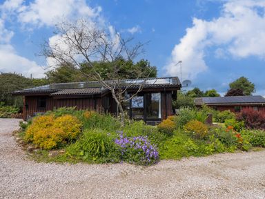 A small wooden house with solar panels on the roof surrounded by shrubs and flowers with a gravel driveway at Greengarth in Yanwath near Penrith