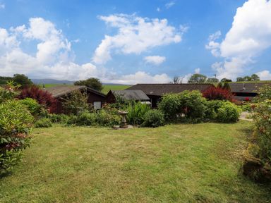 A garden with green grass and plants with houses in the background at Greengarth in Yanwath near Penrith