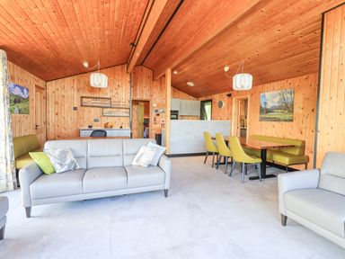 A living room with wooden walls and ceiling a gray sofa green dining chairs and a wooden dining table at Greengarth in Yanwath near Penrith