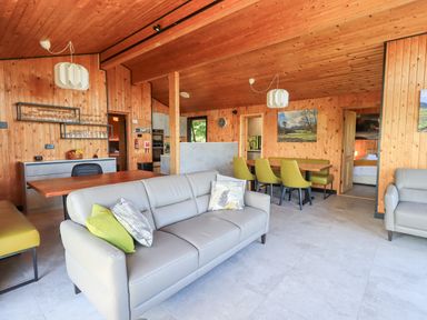 A living room with two gray sofas green chairs wooden walls and ceiling at Greengarth in Yanwath near Penrith