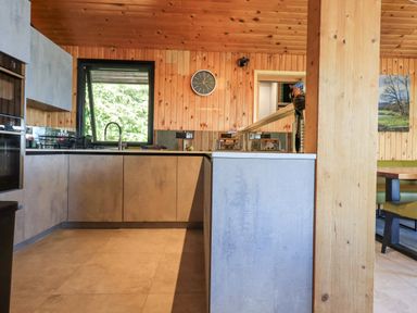 A kitchen with wooden walls and ceiling a black framed window a wall clock and modern cabinetry at Greengarth in Yanwath near Penrith