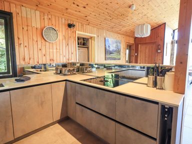 A kitchen with grey cabinets a clock on the wooden wall and kitchen utensils on the counter at Greengarth in Yanwath near Penrith