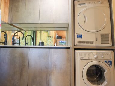 A laundry area with a washing machine and dryer next to cabinets and a sink with black faucets at Greengarth in Yanwath near Penrith