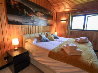 A bedroom with a large bed pillows folded towels bedside lamp and landscape painting on wooden walls at Greengarth Yanwath near Penrith