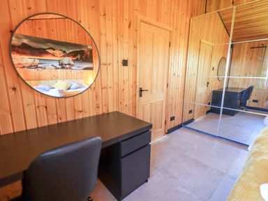 A room with wooden walls a black desk and chair a round mirror and a mirrored wardrobe at Greengarth in Yanwath near Penrith