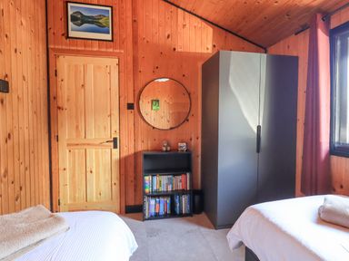 A bedroom with wooden panel walls two beds with white linens a black wardrobe a small black bookshelf and a round mirror at Greengarth in Yanwath near Penrith