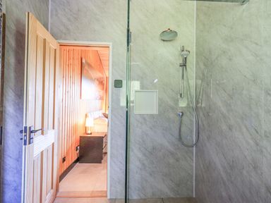 A bathroom with a shower and a wooden door opening to a bedroom with wooden walls and a bedside table with a lamp at Greengarth in Yanwath near Penrith