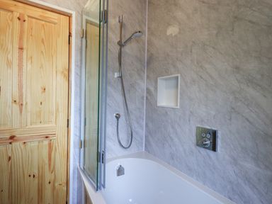 A bathroom with a white bathtub glass shower screen a handheld showerhead and a wooden door at Greengarth in Yanwath near Penrith