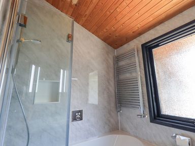 A bathroom with a shower area glass screen showerhead window and towel radiator at Greengarth in Yanwath near Penrith