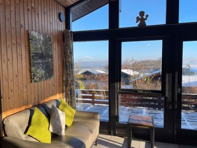 A sitting area with a gray sofa with green and beige cushions next to large windows and a small wooden table at Greengarth in Yanwath near Penrith