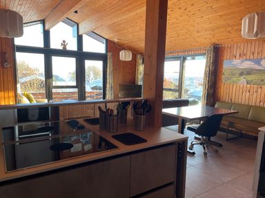 A kitchen with stovetop and utensils overlooking a dining area with a table chairs and sofa and large windows at Greengarth in Yanwath near Penrith