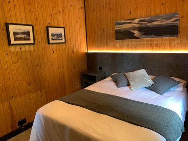 A bedroom with a bed made with white linens and grey pillows with wooden walls and framed pictures at Greengarth in Yanwath near Penrith