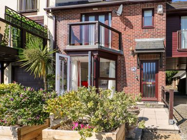 Front view of a brick house with glass balcony wooden planters with green plants and an open glass door at Yacht Haven View in Neyland