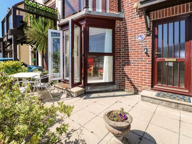An outdoor patio area with a table and chairs next to a brick building with glass doors open at Yacht Haven View in Neyland
