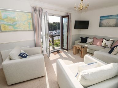A living room with sofas a small wooden table a wall-mounted TV and open doors leading to a marina view at Yacht Haven View in Neyland