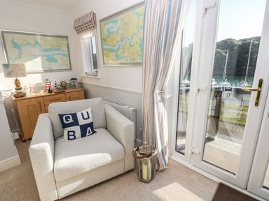 A small living area with an armchair and cushion near glass doors overlooking a marina at Yacht Haven View in Neyland