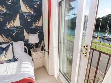 A bedroom corner with a bed next to a nightstand and glass doors opening to a view of water and boats at Yacht Haven View in Neyland