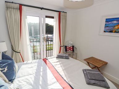 A bedroom with a bed towels on it sliding glass doors and curtains a chair with a cushion and a wooden table at Yacht Haven View in Neyland