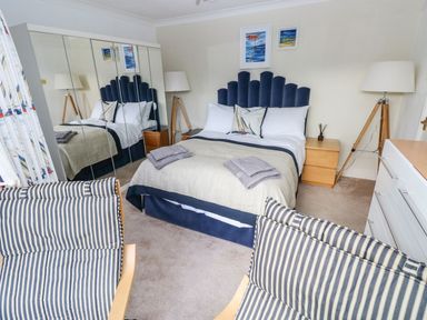 A bedroom with a double bed two bedside tables two lamps a dresser a mirrored wardrobe and striped chairs at Yacht Haven View in Neyland