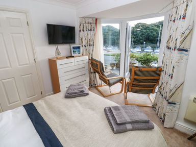 A bedroom with a bed and towels a chest of drawers with a tv and two chairs near a window at Yacht Haven View in Neyland