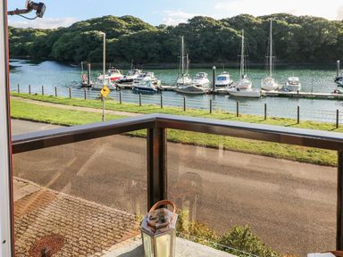 A view of boats docked on water with trees in the background seen from a balcony with a glass railing and a lantern at Yacht Haven View in Neyland