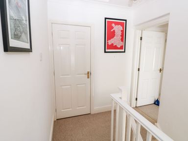 A hallway with white doors beige carpet and framed pictures on the walls at Yacht Haven View in Neyland