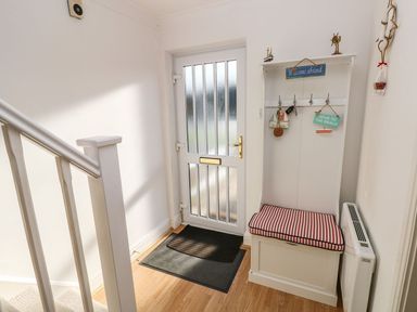 A hallway with a white door a white bench with a red and white cushion and hooks for keys at Yacht Haven View in Neyland