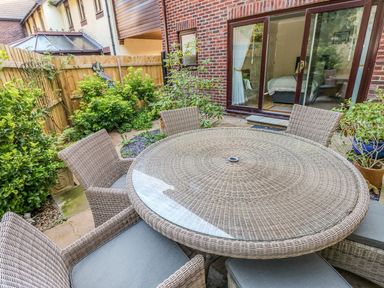 A patio with a round wicker table and wicker chairs near a brick house with sliding glass doors at Yacht Haven View in Neyland