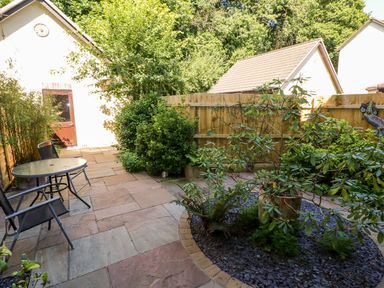 A garden patio with a round glass table and two chairs surrounded by plants and shrubs at Yacht Haven View in Neyland