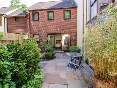 A paved backyard with plants and patio furniture in front of a brick house with sliding glass doors at Yacht Haven View in Neyland