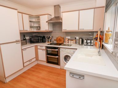 A kitchen with white cabinets a washing machine oven microwave toaster kettle and a sink at Yacht Haven View in Neyland