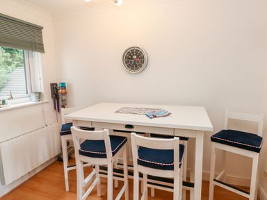 A dining area with a white table and four chairs with blue cushions and a wall clock at Yacht Haven View in Neyland