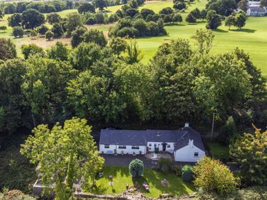 An aerial view of a white house with a garden surrounded by trees and a grassy landscape at Ty Bach - Beaumaris in Beaumaris