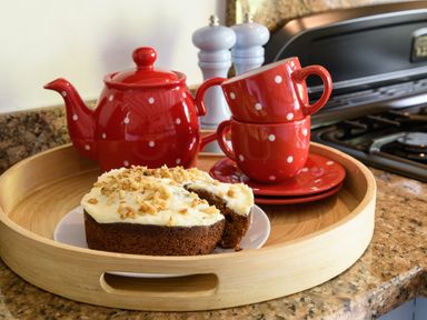 A kitchen tray with a red teapot, two stacked red polka dot cups with saucers, and a cake with white frosting and nuts at Ty Bach - Beaumaris in Beaumaris