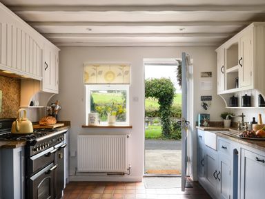 A kitchen with a stove a window with flowers an open door showing a garden at Ty Bach - Beaumaris in Beaumaris