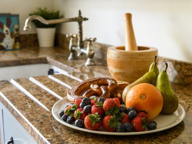 A kitchen counter with a plate of strawberries blueberries pears grapefruit and pretzel alongside a wooden mortar and pestle at Ty Bach - Beaumaris in Beaumaris